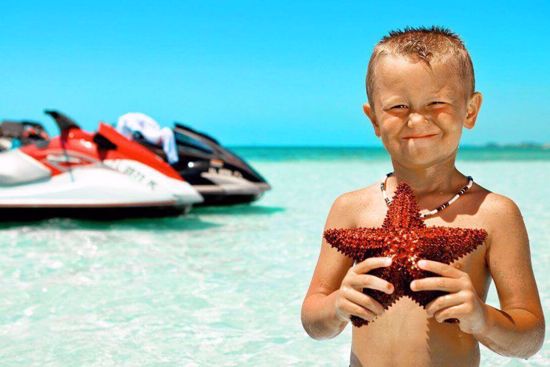 Child holding a starfish on a beach with jet skis in the background while on vacation in Key West Florida.
